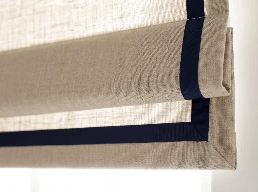 Close up of a beautifully crafted Roman blind featuring a contrasting dark border ribbon.